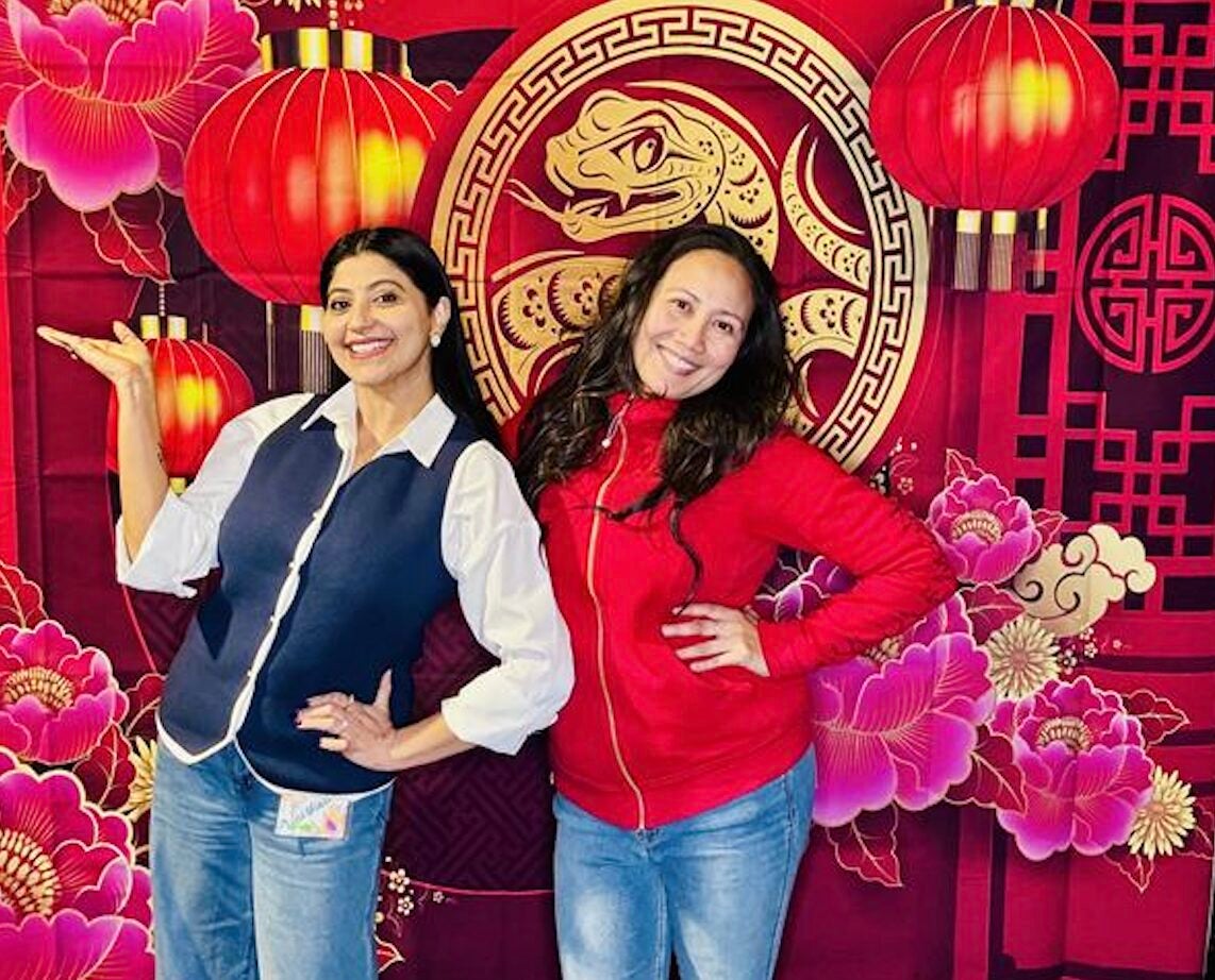 Two women posing in front of a Lunar New Year banner